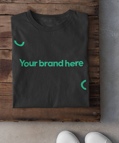 En svart t-shirt ligger vikt på bordet med texten "brand merch made easy" på.